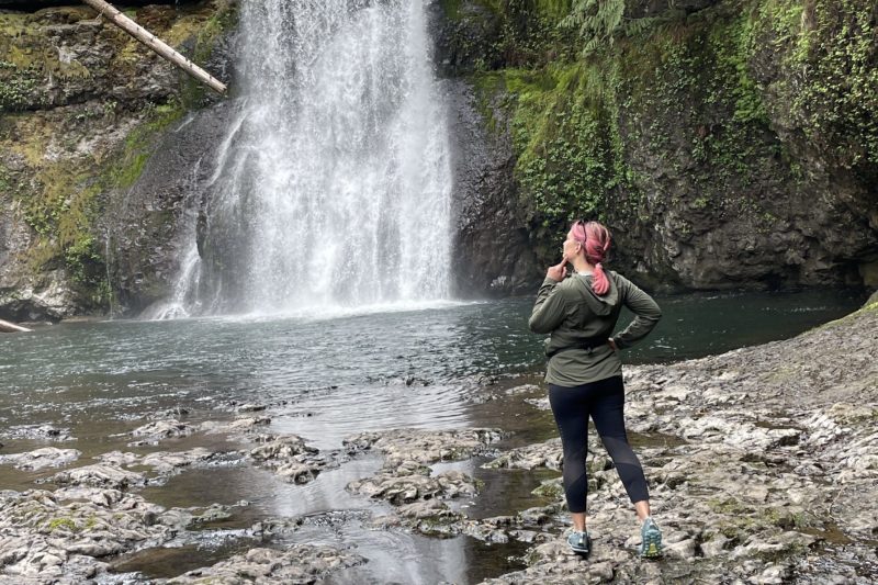 girl with pink hair in front of a waterfall
