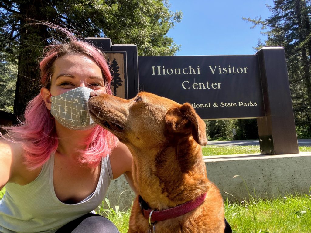 A dog and her owner in front of Redwood National Park sign, looking for dog-friendly hikes