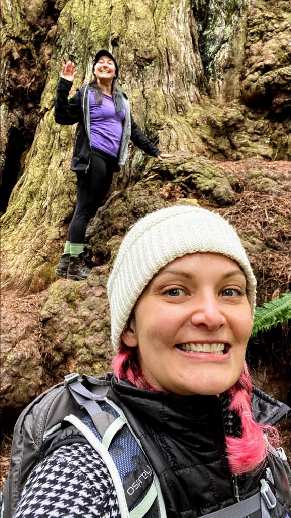 two women in front of a tall tree