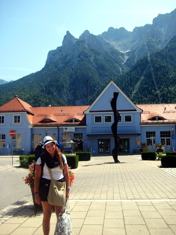 A young woman laden with bags waiting outside a train station on a budget travel trip