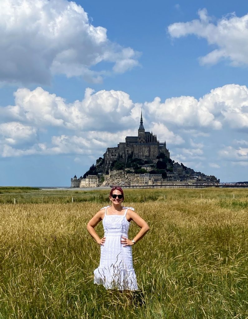 A girl in a white dress with bright pink hair enjoys a trip to Mont St. Michel in France