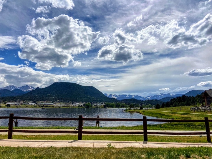image shows estes park lake behind a small trail and fence, with mountains behind it