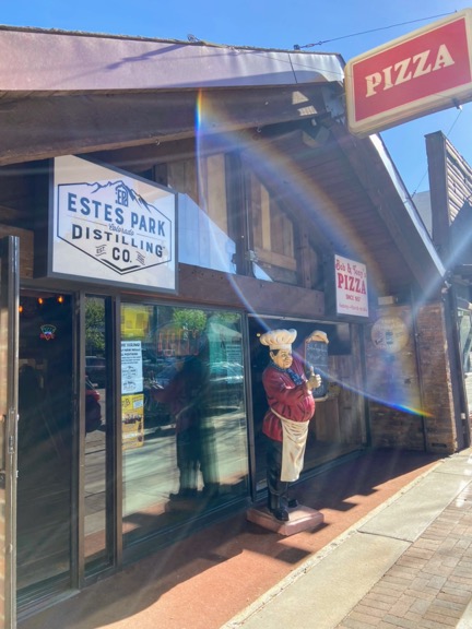 image shows a pizza restaurant in estes park, colorado, where rocky mountain national park is. a fake italian chef statue is out front. a lens flare artfully frames the image.