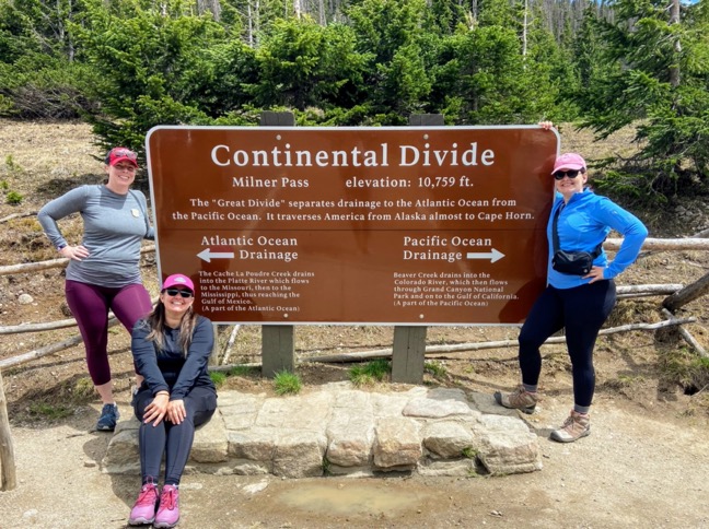 image shows three lovely women standing around a large metal roadside sign that says Continental Divide, elevation 10,759 feet.