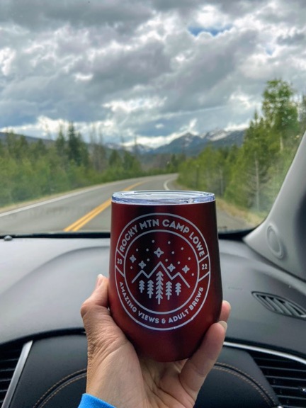 image shows a red wine tumbler being held inside a car while driving on a mountainous road. the holder of the wine mug is not driving.