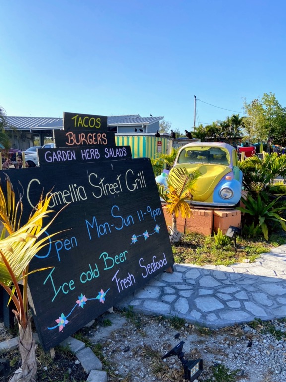 image shows a chalkboard with a menu written on it in front of an old yellow VW beetle in Everglades City