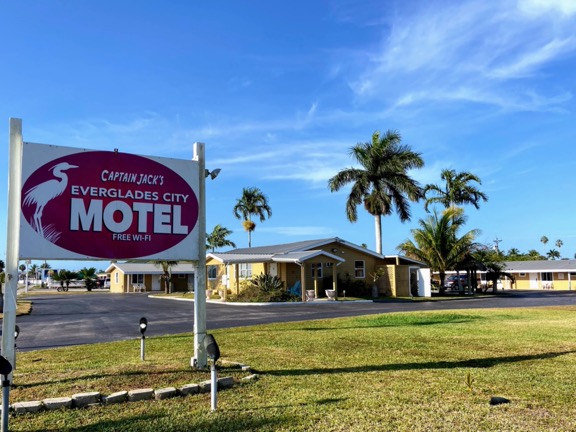 image shows a sign for Everglades City Motel in front of a yellow motel with palm trees and a blue sky