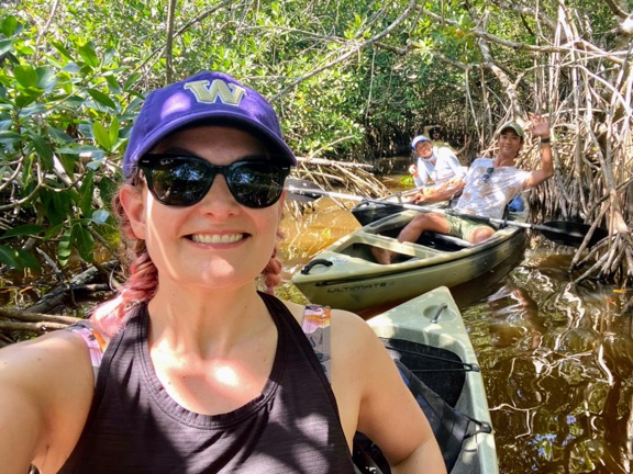 image shows a woman with pink hair taking a selfie with two other people all in kayaks in mangroves