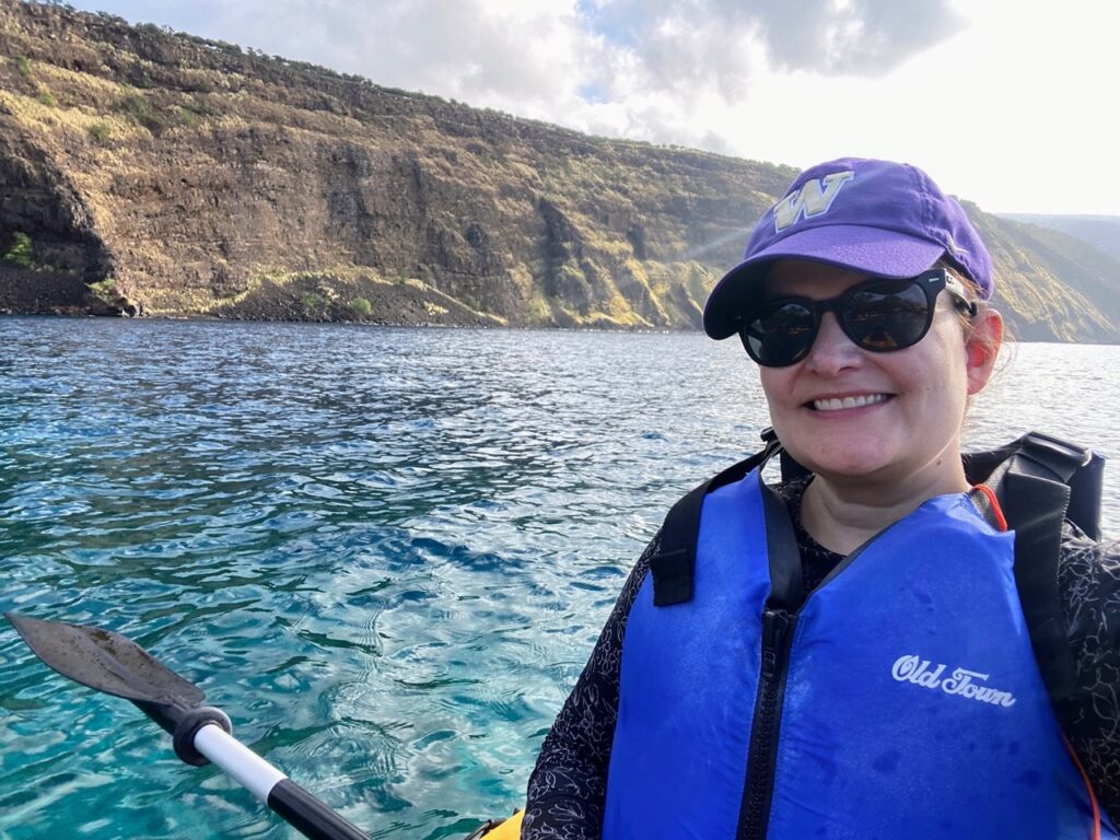 image shows a woman kayaking in a purple hat and blue life jacket in blue water, part of a five day itinerary focused on national parks on the Big Island of Hawaii