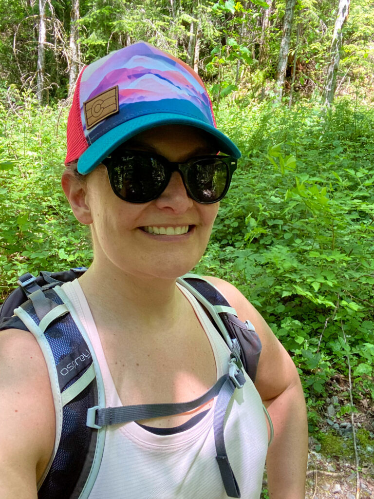 image shows a woman in a brightly colored hat hiking using Trailhead Direct