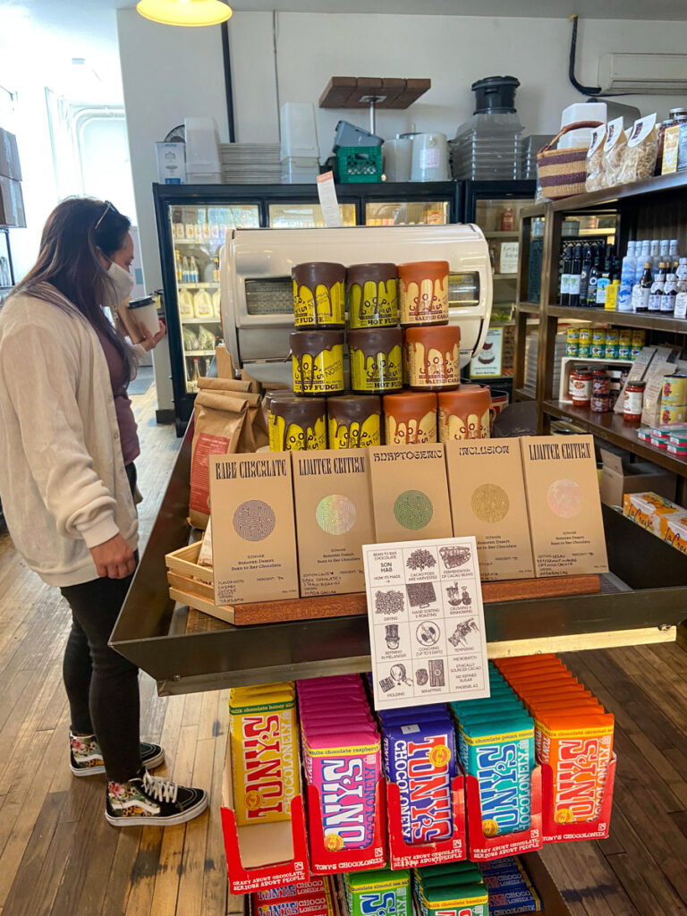 a woman in a white shirt and jeans shops at a local market with candy bars and foodstuffs in tucson