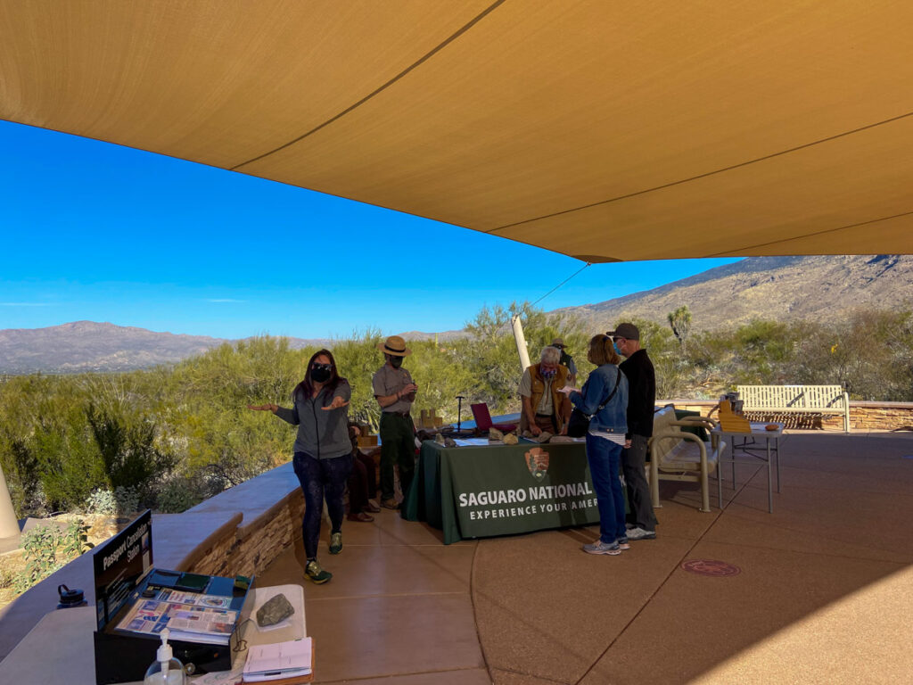 the visitor center at Saguaro NP. Rangers stand around an outdoor table while guests ask questions.
