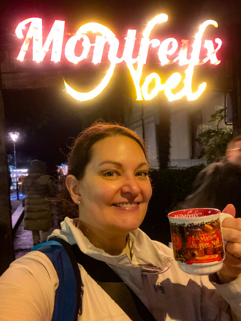 image shows a woman beneath a lit up Montreux Noel sign with a cup of mulled wine