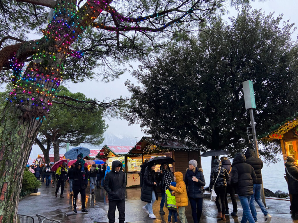 People in winter coats with umbrella walk along the Montreux Christmas market huts in the rain