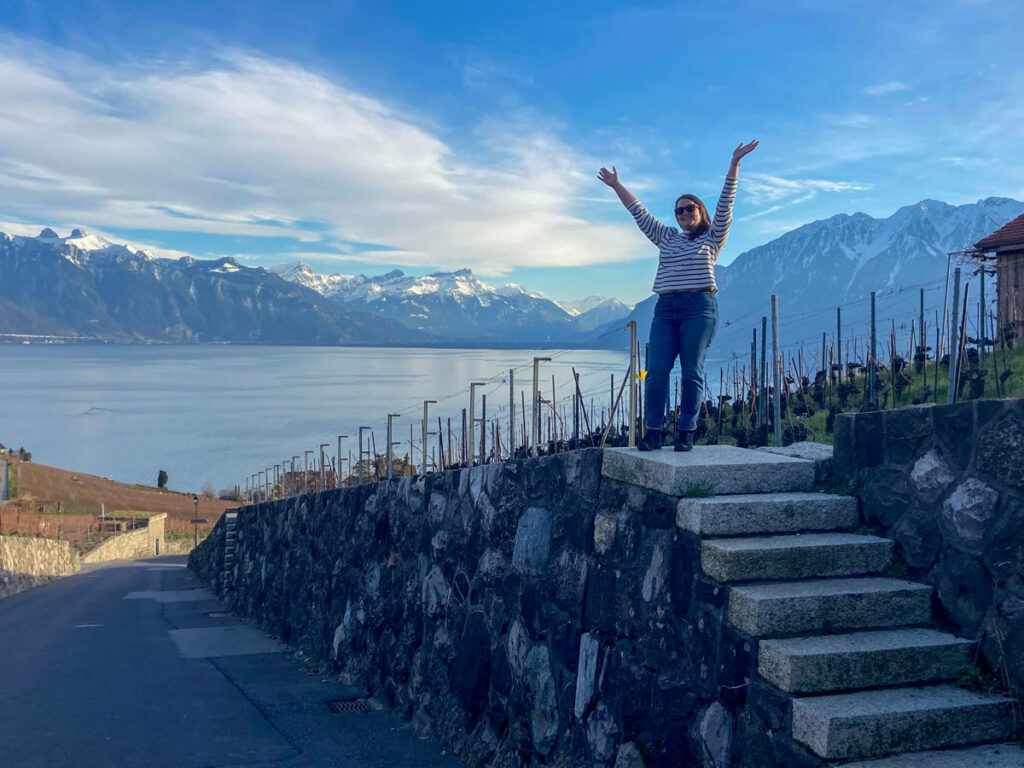 image shows a woman standing on small steps in front of lake geneva in the lavaux vineyard region in the winter