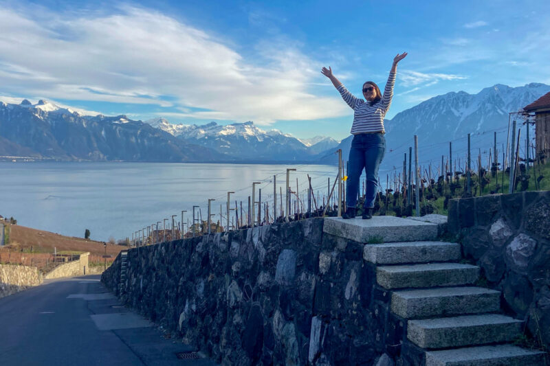 image shows a woman standing on small steps in front of lake geneva in the lavaux region