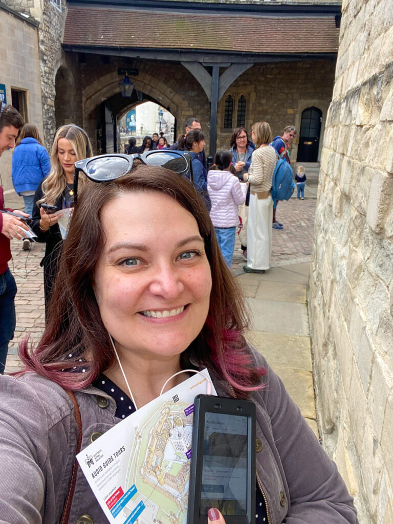 a woman with pink and brown hair gleefully shows off her audio tour device at the tower of london