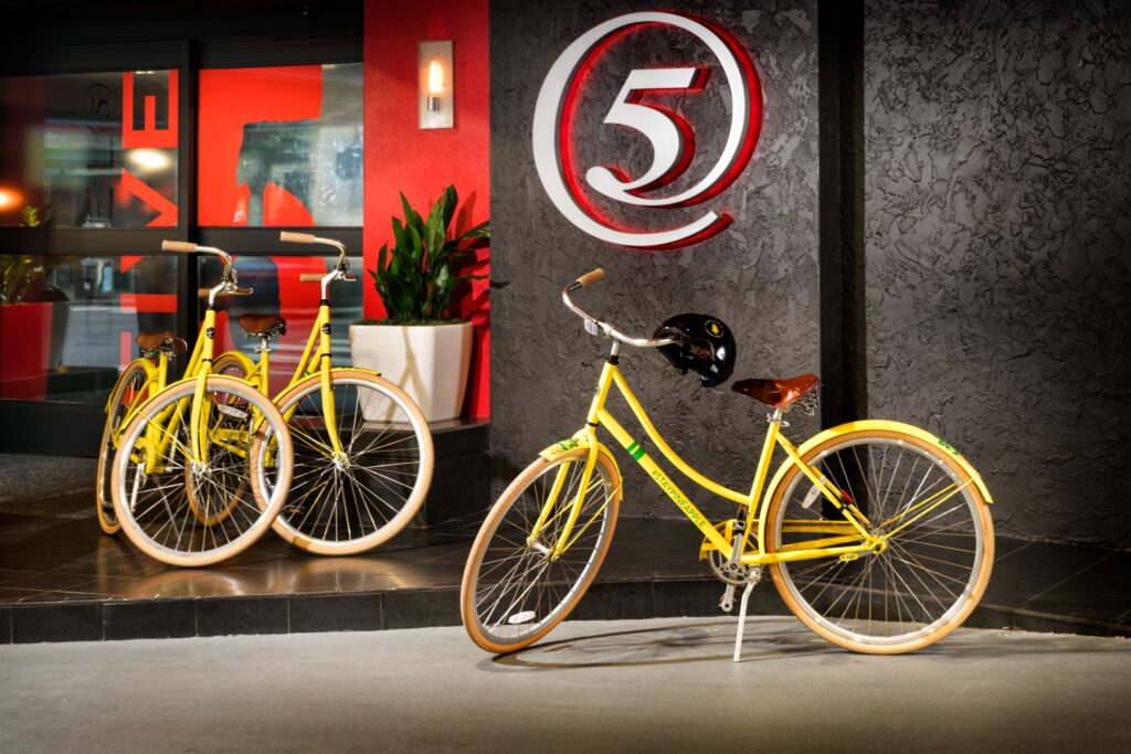 three bright yellow bikes are propped in front of a sign of the number five
