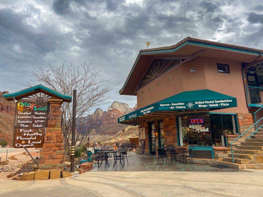 A nondescript cafe building for Cafe Soleil in Springdale, with a green awning. Behind are the rocks of Zion